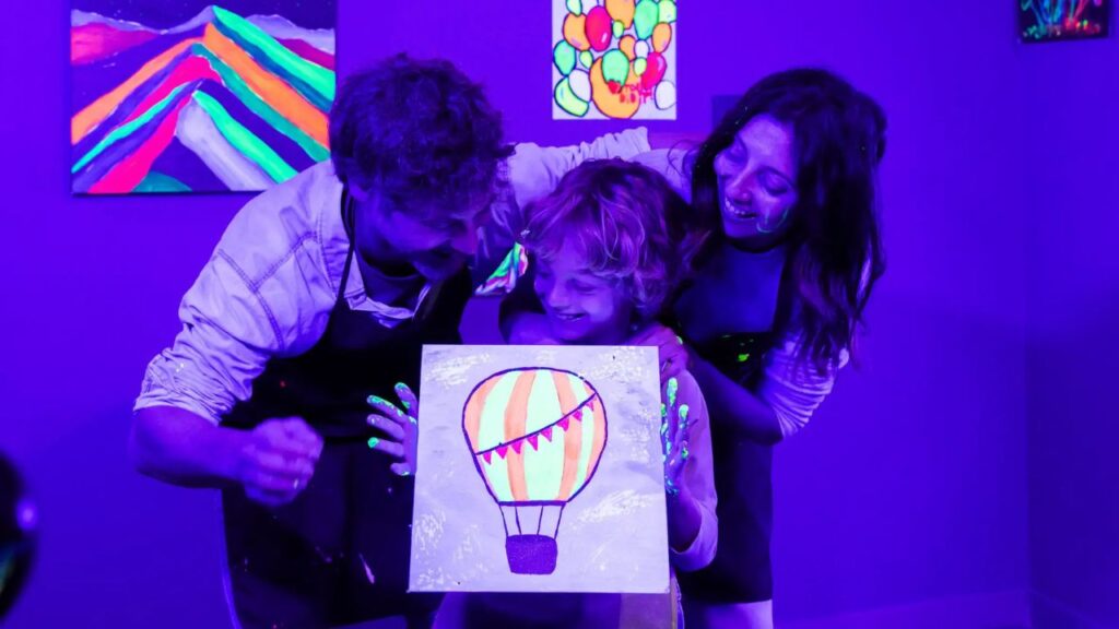 Padre, madre e hijo disfrutando juntos en un taller de pintura fluorescente en Neon Brush Kids.