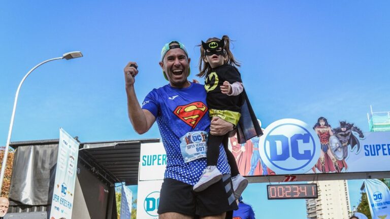 Padre con camiseta de Superman sostiene a su hija disfrazada de Batgirl en la meta de la DC Super Heroes Run Madrid.
